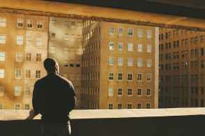 man standing on rooftop facing brown highrise building